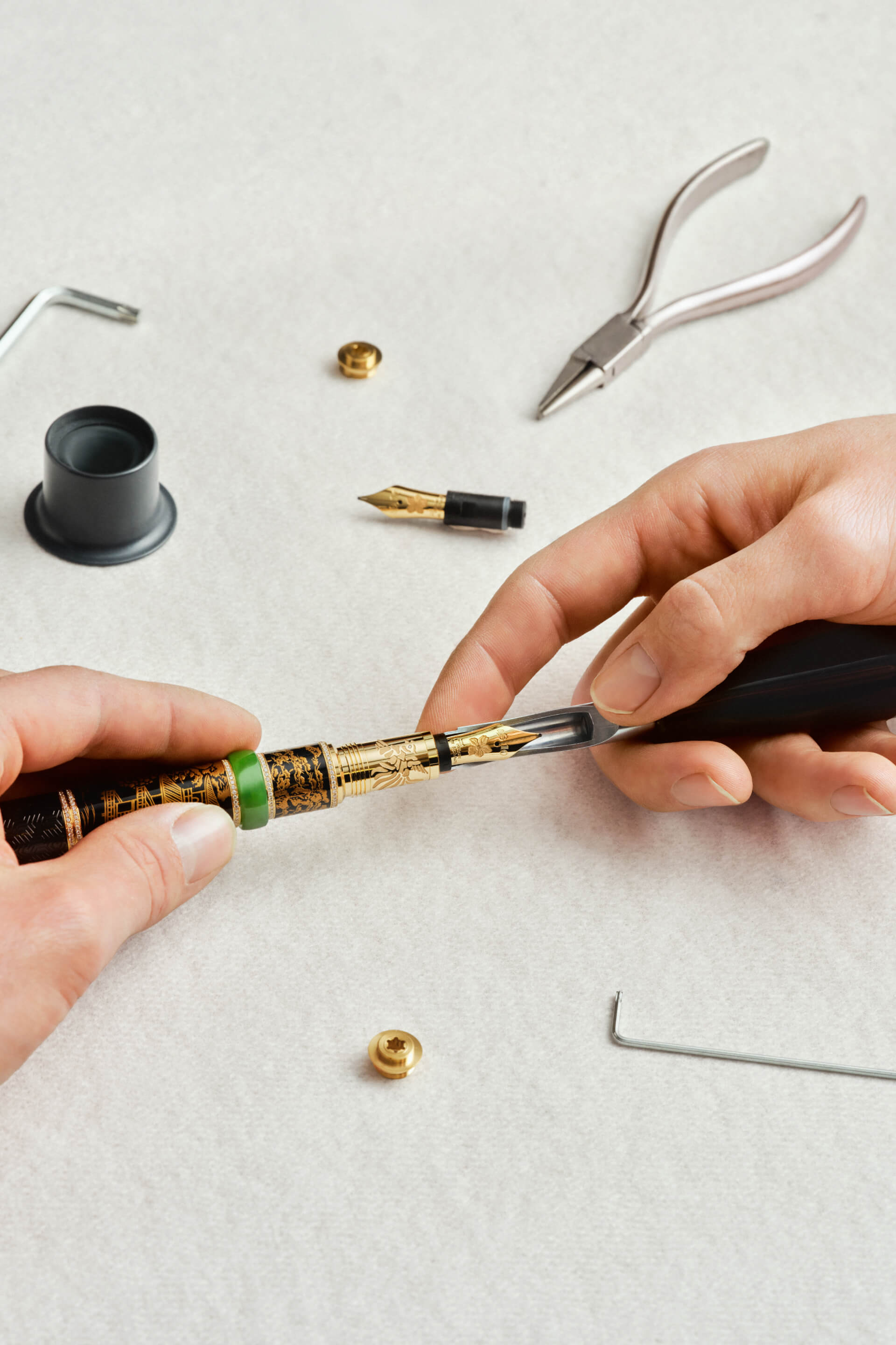 Montblanc engraved fountain pen with gold accents and a green ring, hands assembling the gold nib in close-up.