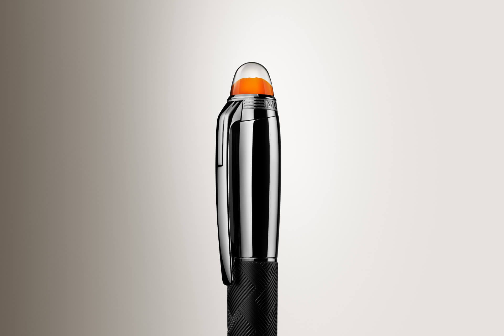 قلم "مون بلان ستار ووكر" (Montblanc Starwalker)؛ يتميز بغطاء داكن لامع، وهيكل أسود ذي ملمس بارز، وشعار برتقالي يبدو عائماً تحت قبة شفافة (لقطة مقربة).