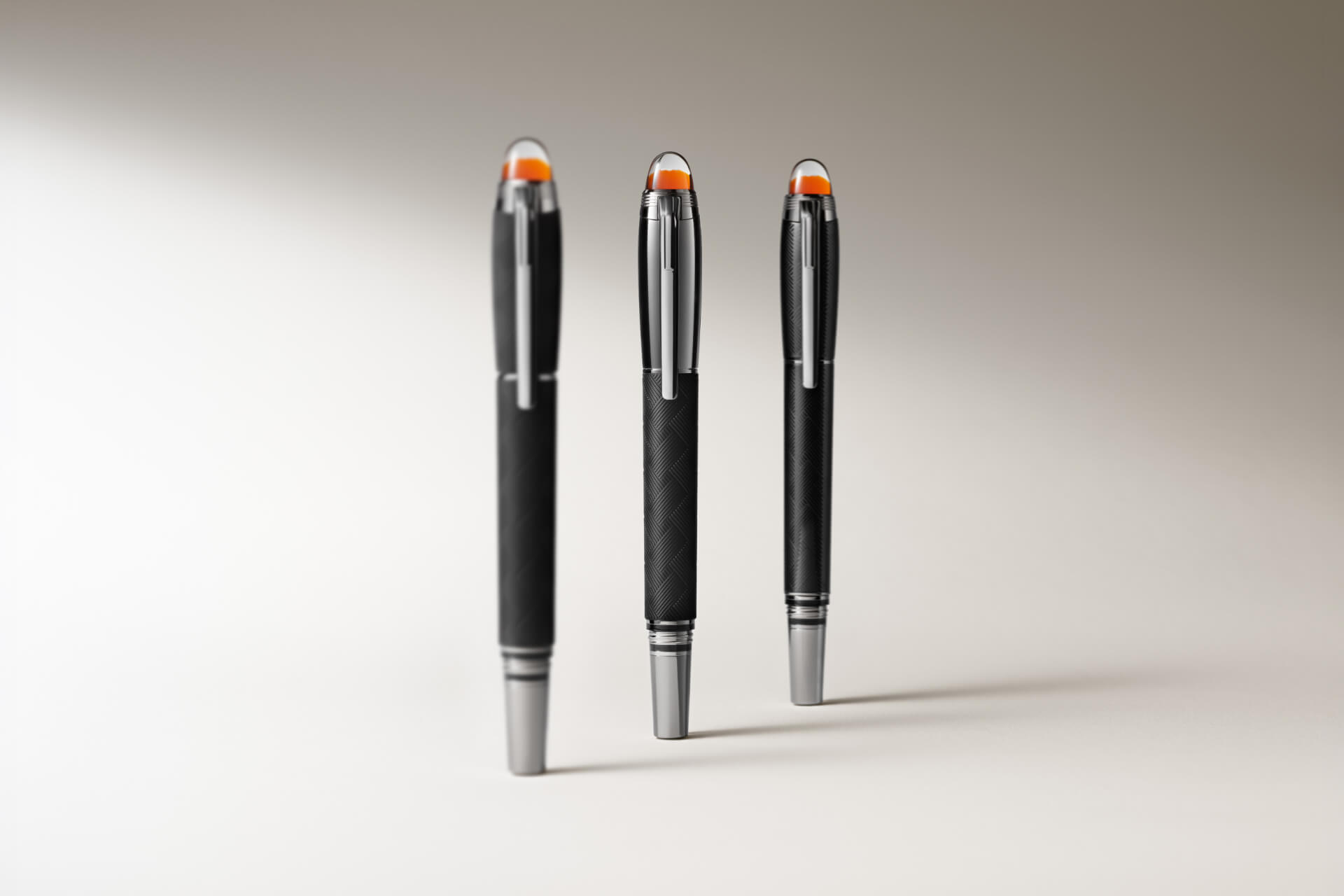 أقلام Montblanc Starwalker: ثلاثة أقلام سوداء ذات أجسام ملمسية، وعناصر تزيينية بلون فضي، ورؤوس علوية نصف شفافة باللون البرتقالي، معروضة بوضعية قائمة على خلفية فاتحة.