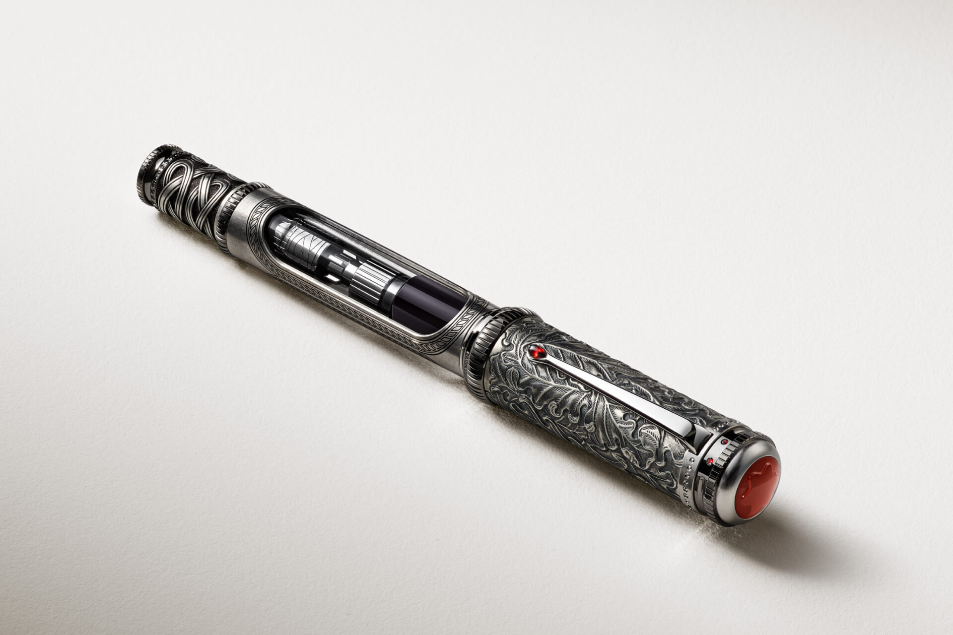 Montblanc fountain pen, intricately engraved silver-toned metal, with visible ink mechanism, red gem on clip, and red star cap, on a white surface.