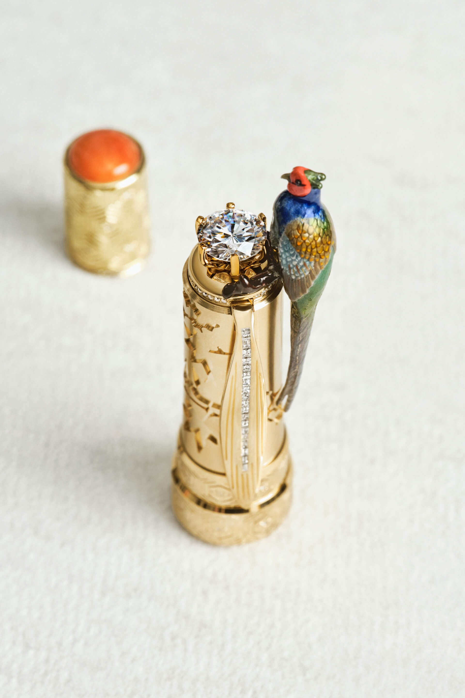 Montblanc luxury fountain pen, ornate gold cap featuring a large diamond finial, diamond-set clip, and vibrant enameled bird figurine, close-up.