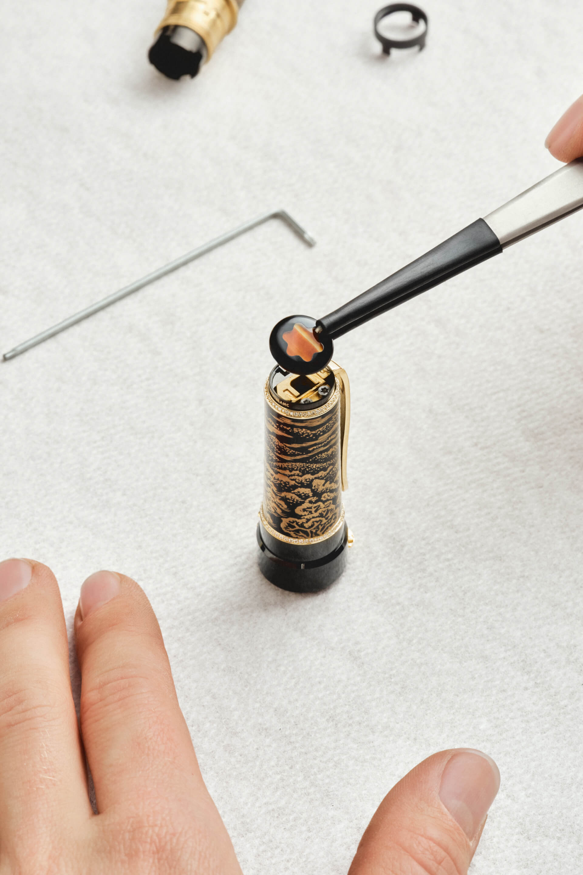 Montblanc fountain pen cap, black and gold patterned, with a diamond band and gold-coated clip, unique Montblanc emblem being carefully placed.