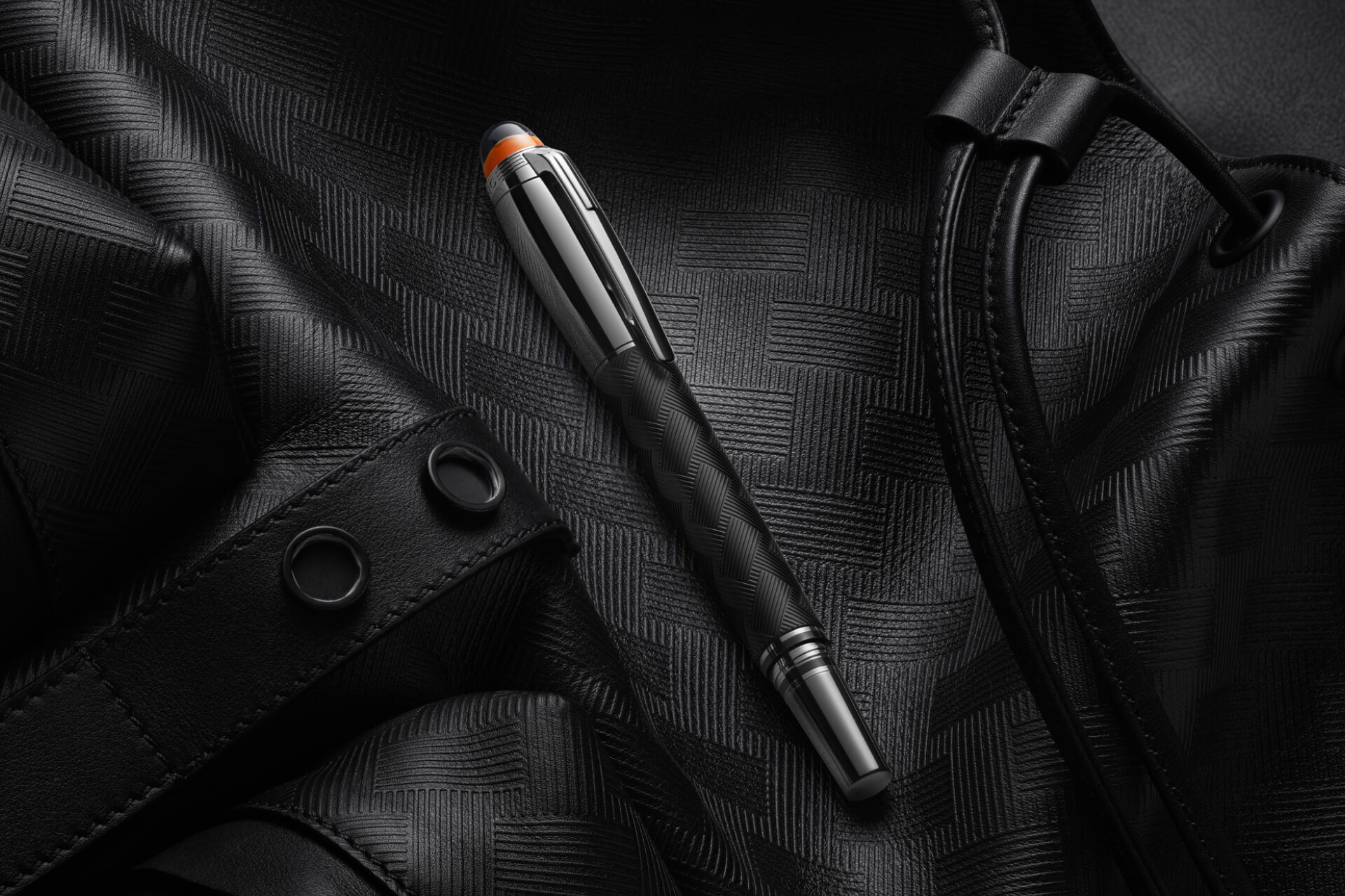 قلم "مون بلان ستار ووكر" (Montblanc Starwalker) بهيكل أسود ذي ملمس بارز، وغطاء معدني، وقبة برتقالية نصف شفافة، معروضاً على سطح من الجلد الداكن المنقوش.
