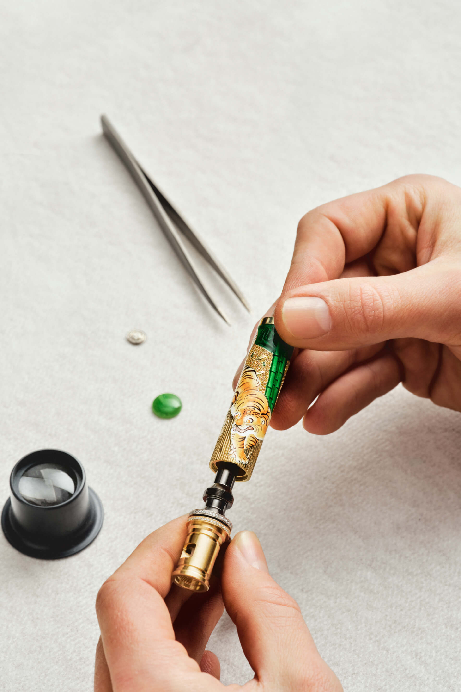 Montblanc luxury writing instrument, golden barrel with intricate hand-painted tiger and bamboo motif, being meticulously assembled by artisan's hands, featuring a diamond-set ring.