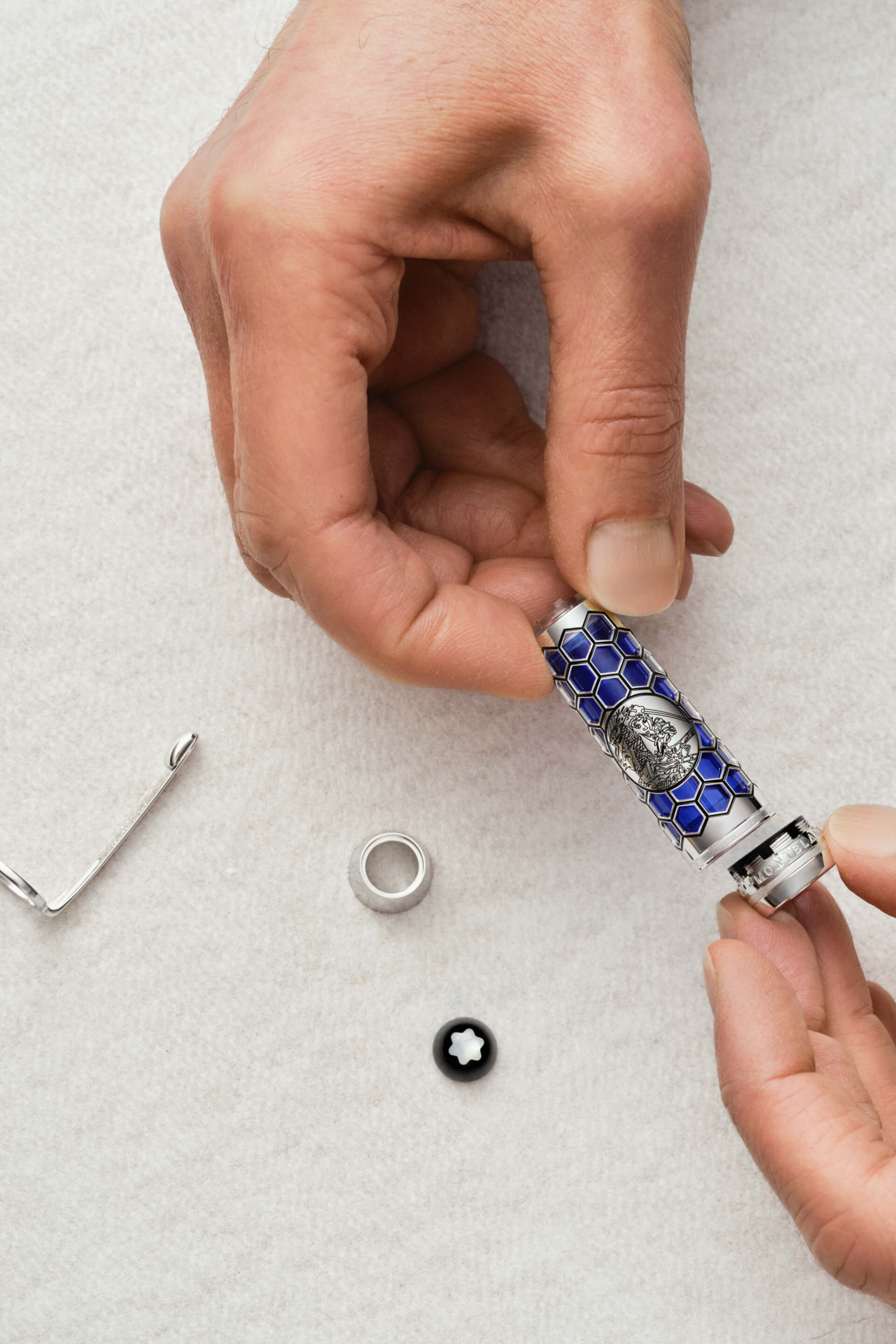 Montblanc pen mechanism with blue reservoir and intricate honeycomb metal casing, held in hands during assembly, snowcap emblem visible.