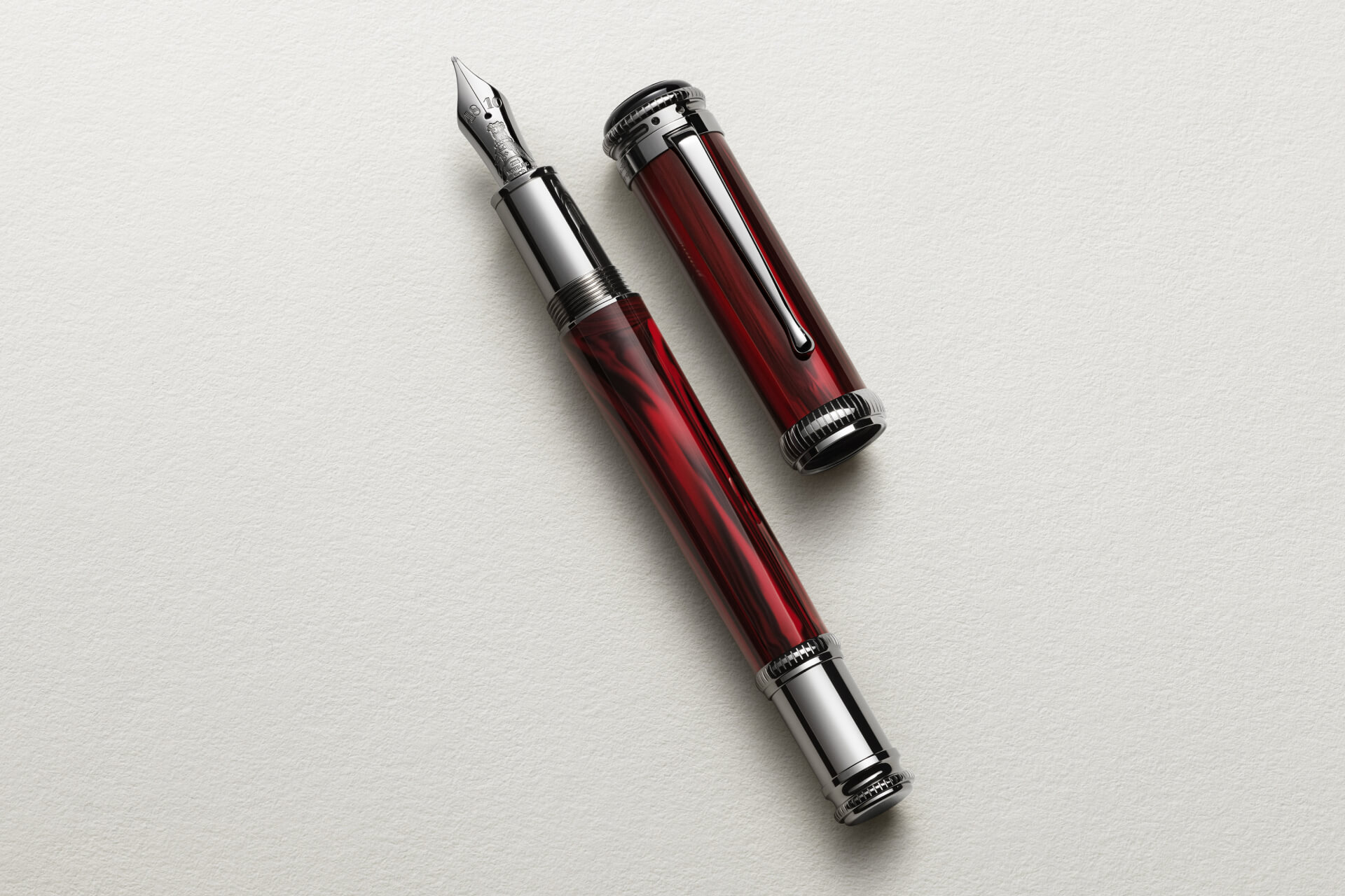 Montblanc fountain pen, rich red marbled resin, platinum-coated fittings, engraved nib, cap alongside barrel on textured white.