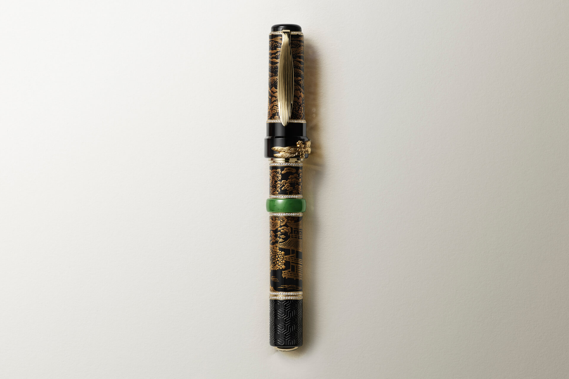 Montblanc ornate fountain pen with black lacquer, detailed gold artistic patterns, crystal-set bands, a sculpted gold dragon, and a vivid green jade ring, captured on a light background.