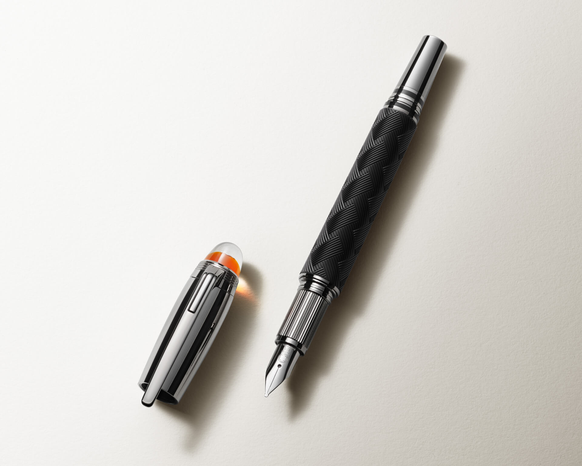 قلم حبر سائل Montblanc Starwalker يتميز بهيكل أسود ذي نقوش، وغطاء مصقول مطلي بالبلاتين، وريشة بلون فضي، وقبة شفافة تضم شعار القمة الثلجية العائم؛ يظهر القلم بدون غطاء وموضوعاً على سطح فاتح اللون.