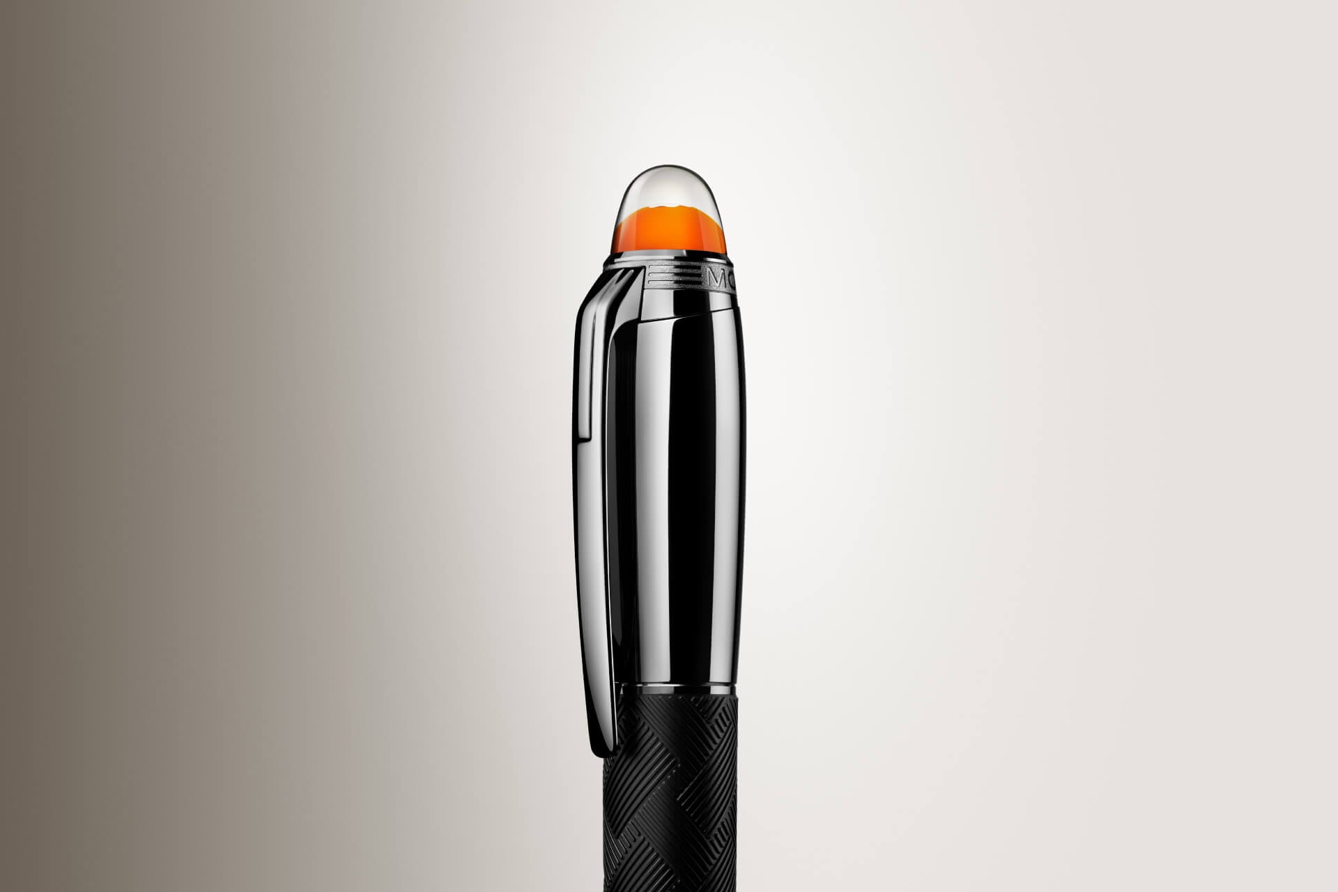 قلم "مون بلان ستار ووكر" (Montblanc Starwalker)؛ يتميز بغطاء داكن لامع، وهيكل أسود ذي ملمس بارز، وشعار برتقالي يبدو عائماً تحت قبة شفافة (لقطة مقربة).