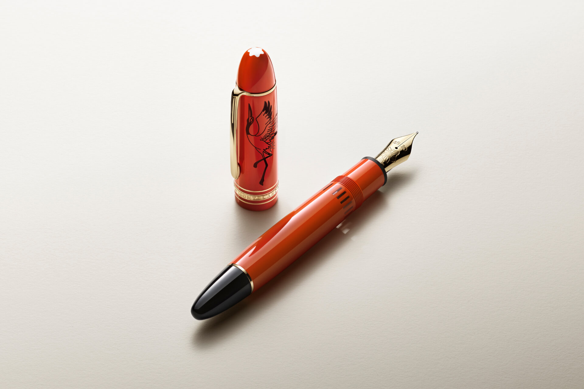 Montblanc fountain pen in vibrant red resin with gold-coated fittings, featuring a black crane design and snowcap emblem on its cap, displayed uncapped.